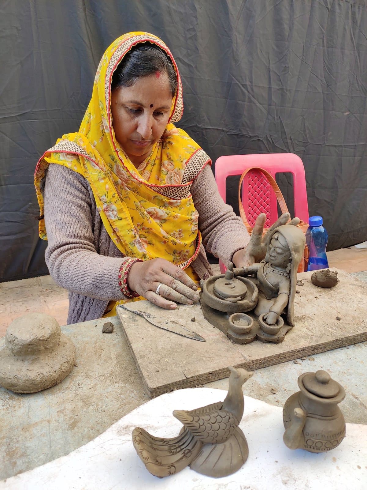 Kailash Devi sculpting a village woman figurine at a traditional stone grinding wheel