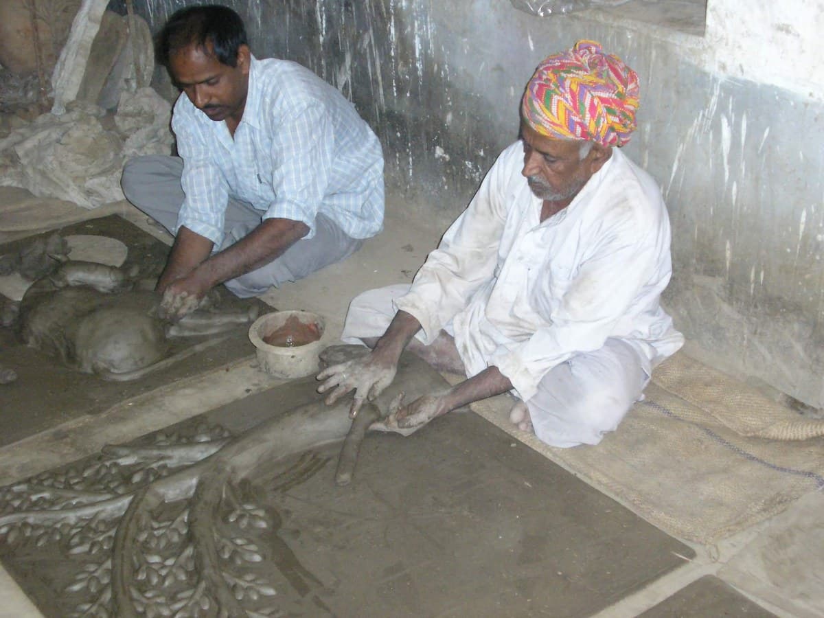 Padma Shri Mohan Lal Kumhar sculpting wet clay relief panels on the workshop floor beside his son Dinesh Chandra Kumhar