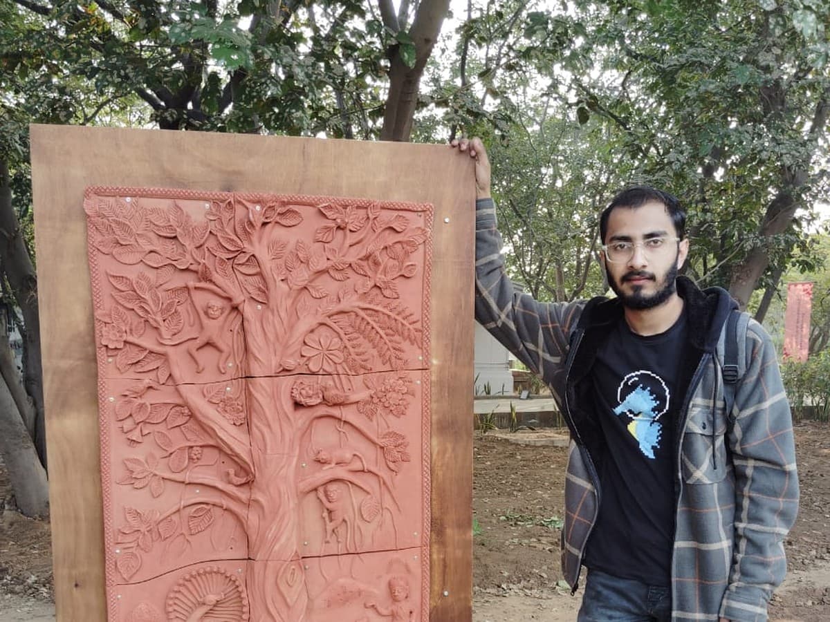 Mohit Kumhar standing beside a handcrafted Tree of Life Molela terracotta relief mural panel